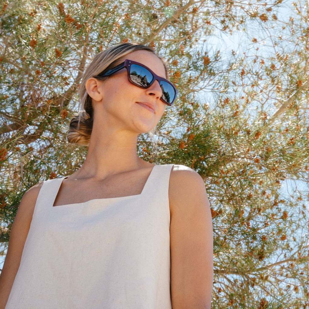Woman in tank top standing under a tree looking to the left wearing sunglasses